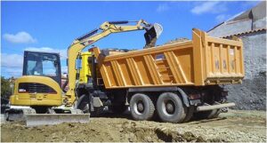Miniexcavadora CAT de excavaciones Félix López cargando tierra en camión para obra pública. La imagen muestra precisión y eficiencia operacional en servicios de excavación, movimiento de tierras y preparación de terrenos ofrecidos por excavaciones Félix López en Castilla y León.